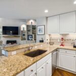 A modern kitchen with granite countertops opens into a stylish living room, featuring elegant furniture and built-in shelves.